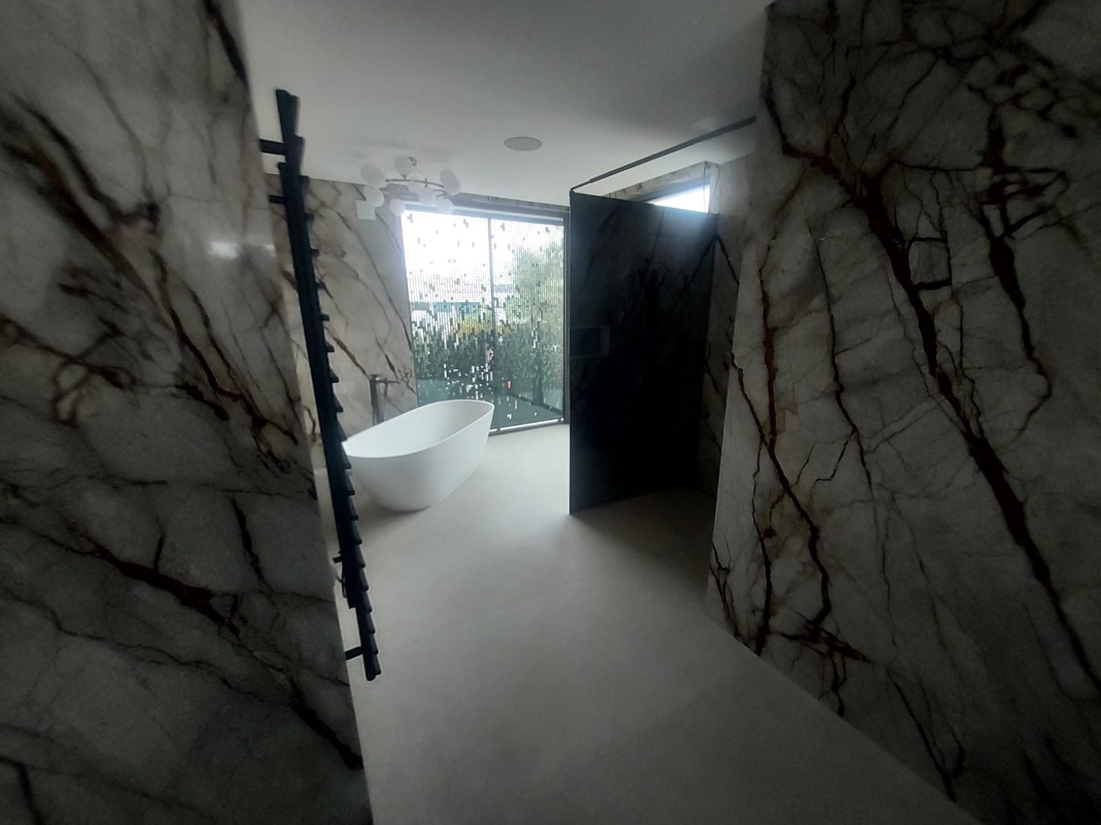 Freestanding bath beside a full-height window in a dark marble bathroom