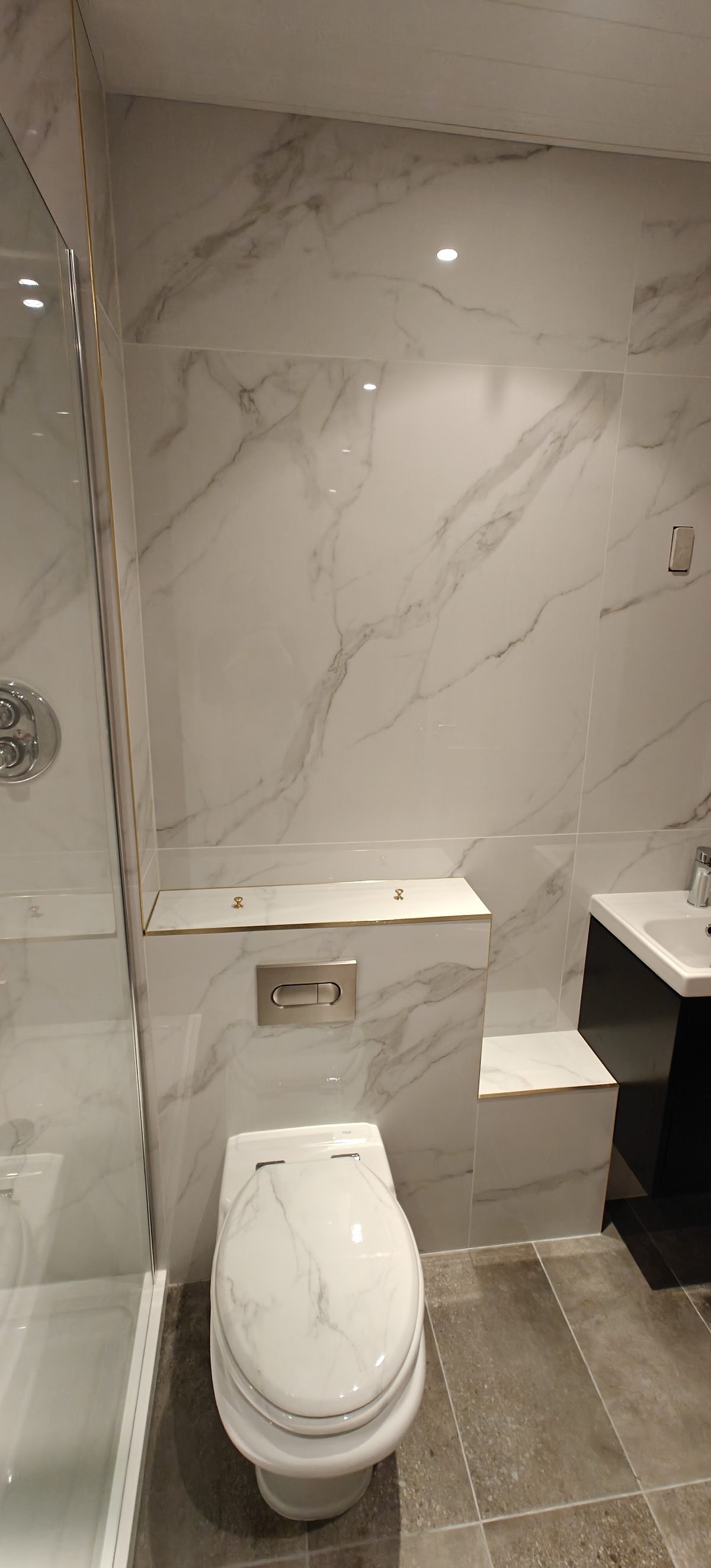 White marble effect tiling around a toilet and dark vanity unit, finished bathroom in Kildare