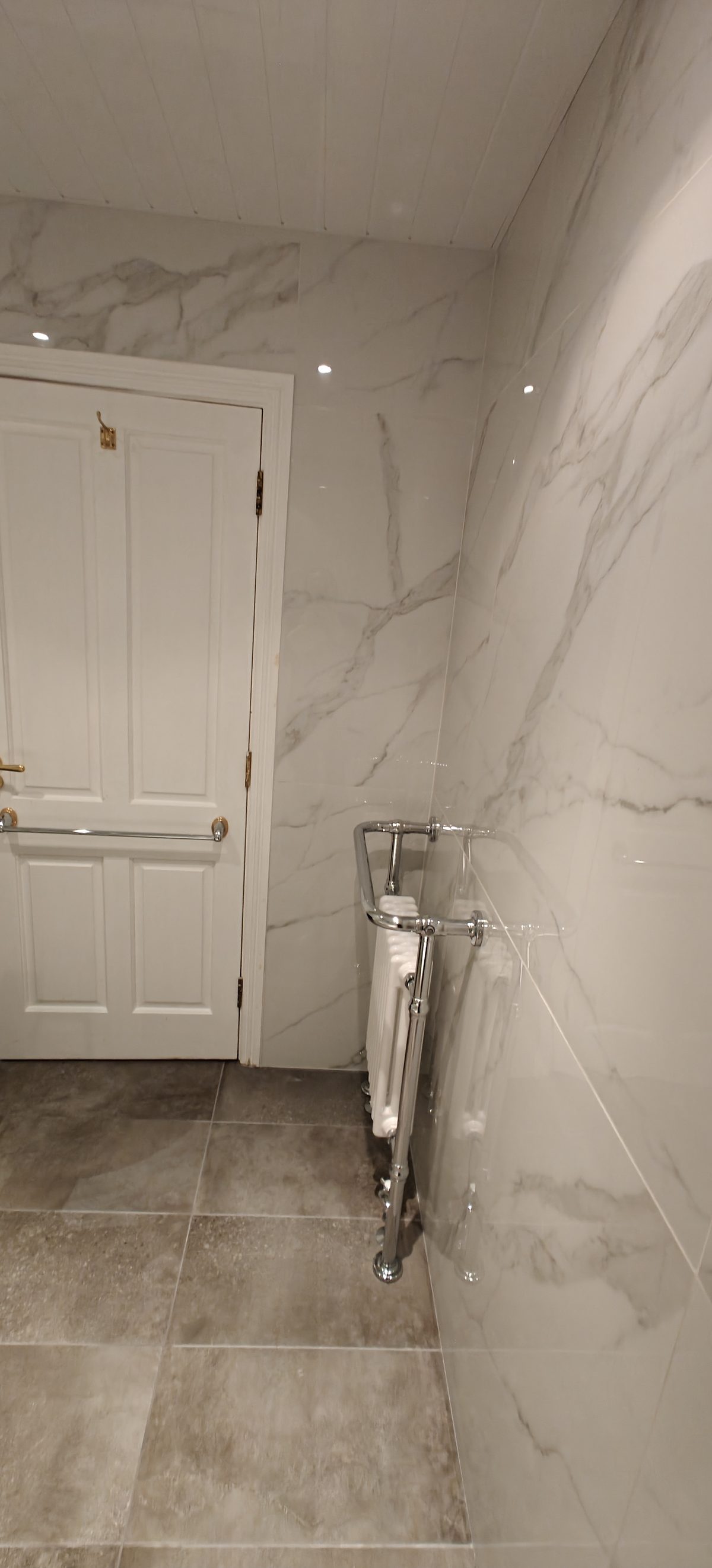 Marble effect bathroom with white panelled door, chrome radiator and grey stone floor