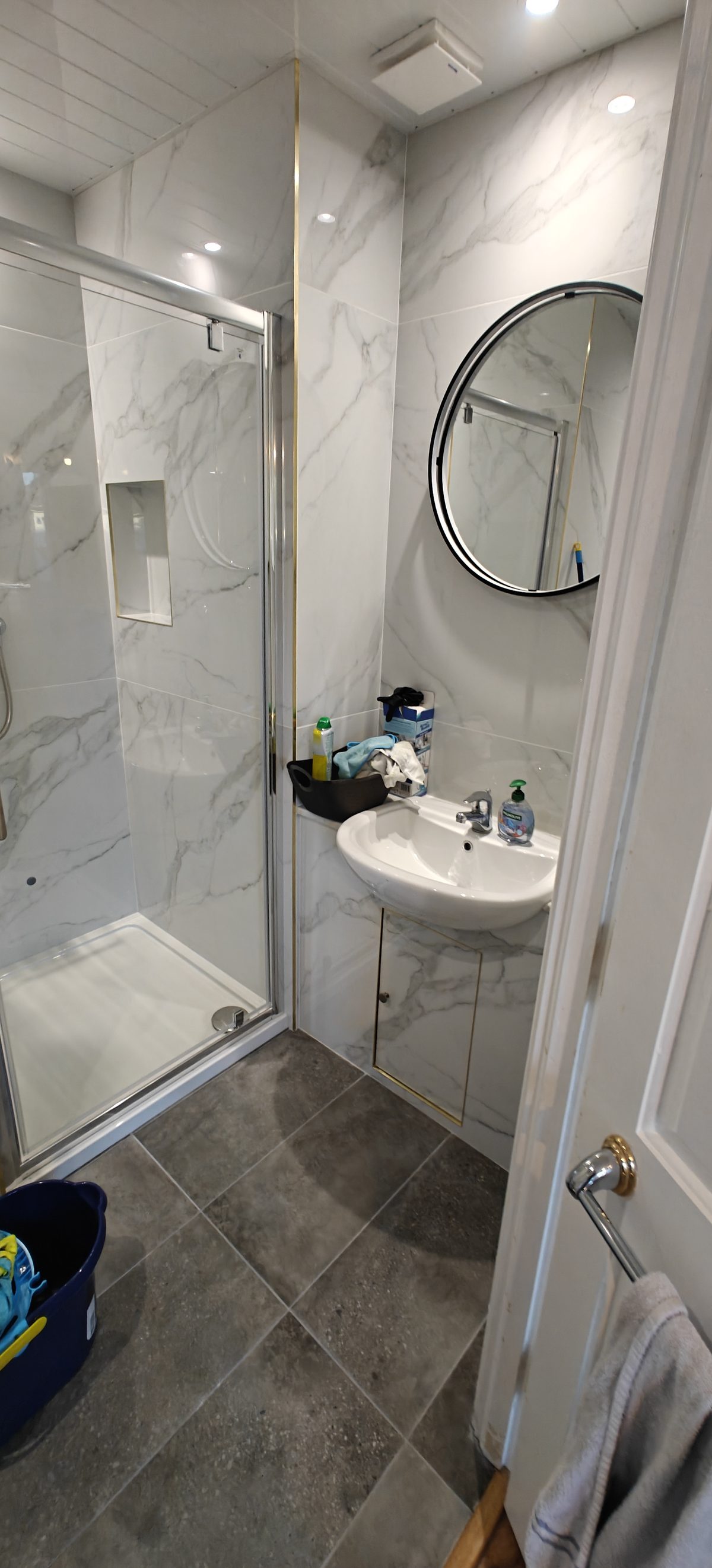 Compact bathroom with marble effect walls, round mirror and dark floor tiles