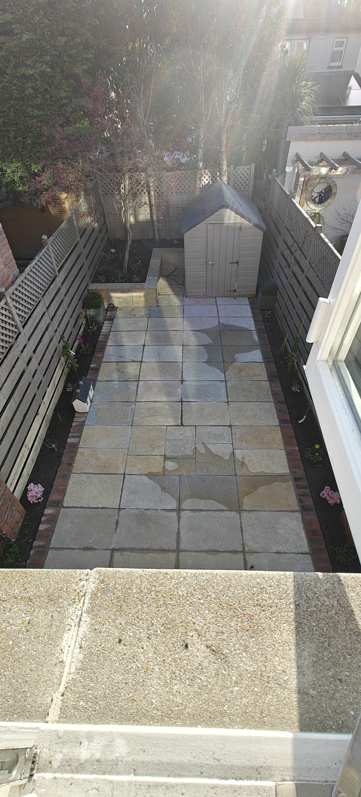 Sandstone patio seen from above with a garden shed and fencing